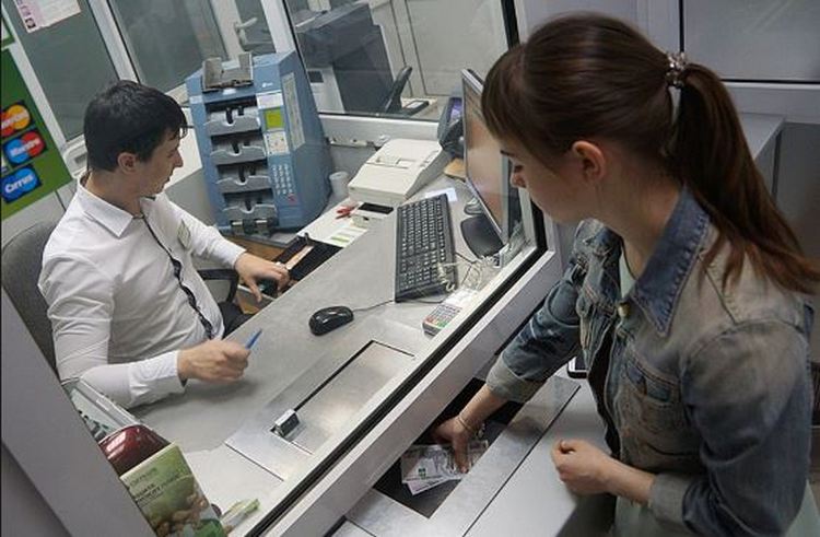 Девушка вносит доллары через кассу банка